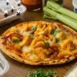 Buffalo chicken tortilla pizza with celery and green onions on a wooden table.
