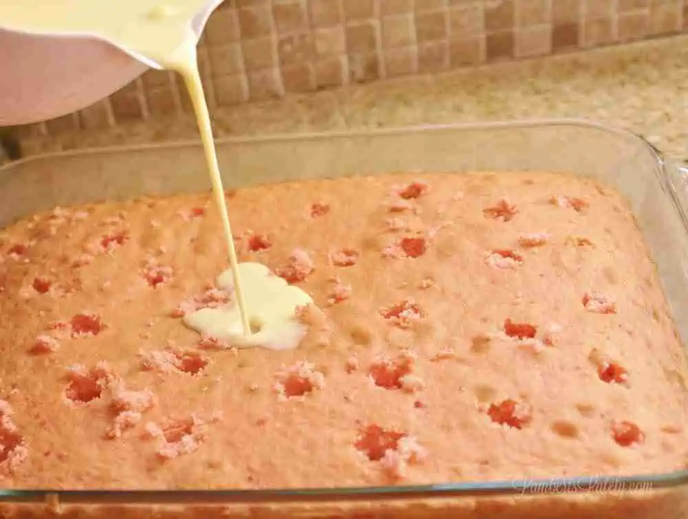 pouring pudding mix over a strawberry cake with holes.