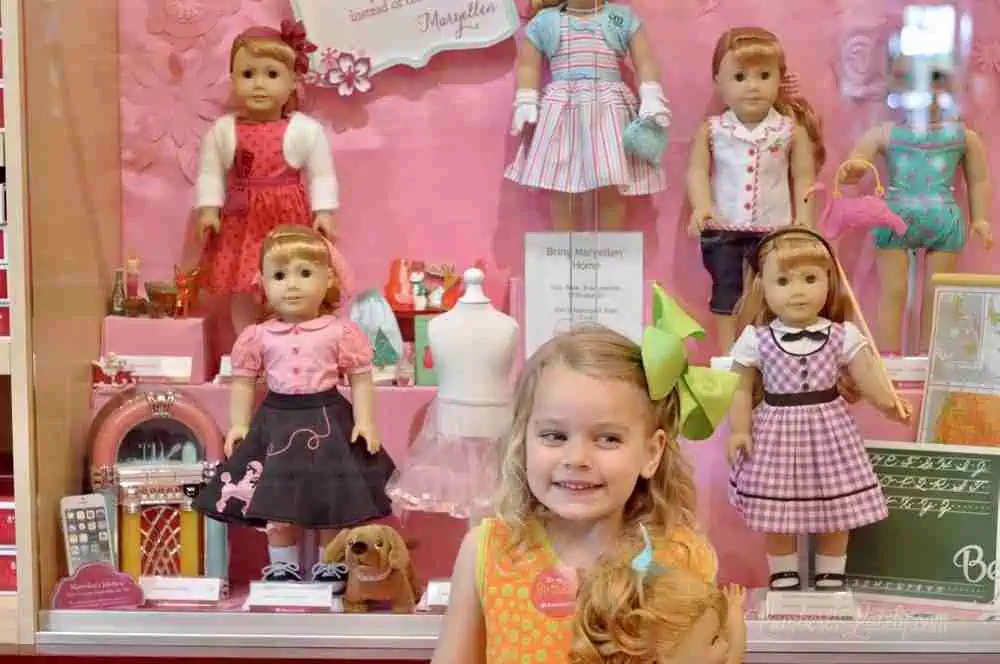 child in american girl store, in front of dolls.