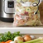 Homemade vegetable broth in a plastic bag with fresh vegetables nearby.