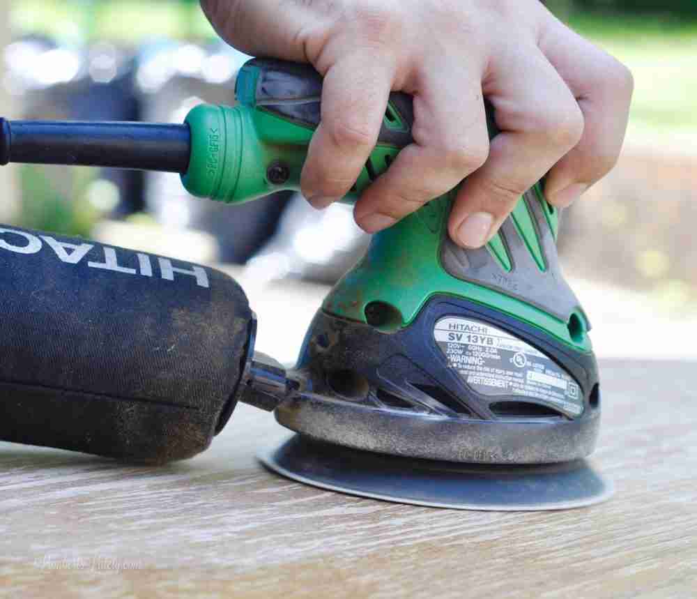 sanding a wood table with an orbital sander.
