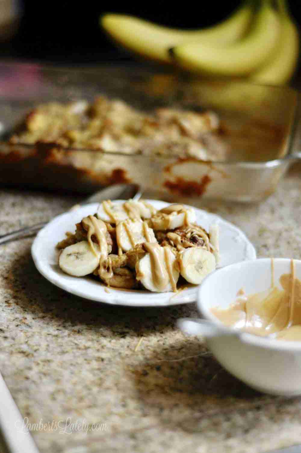 Overnight Monkey French Toast Casserole on a white plate, with baking dish, bananas, and bowl of peanut butter sauce.