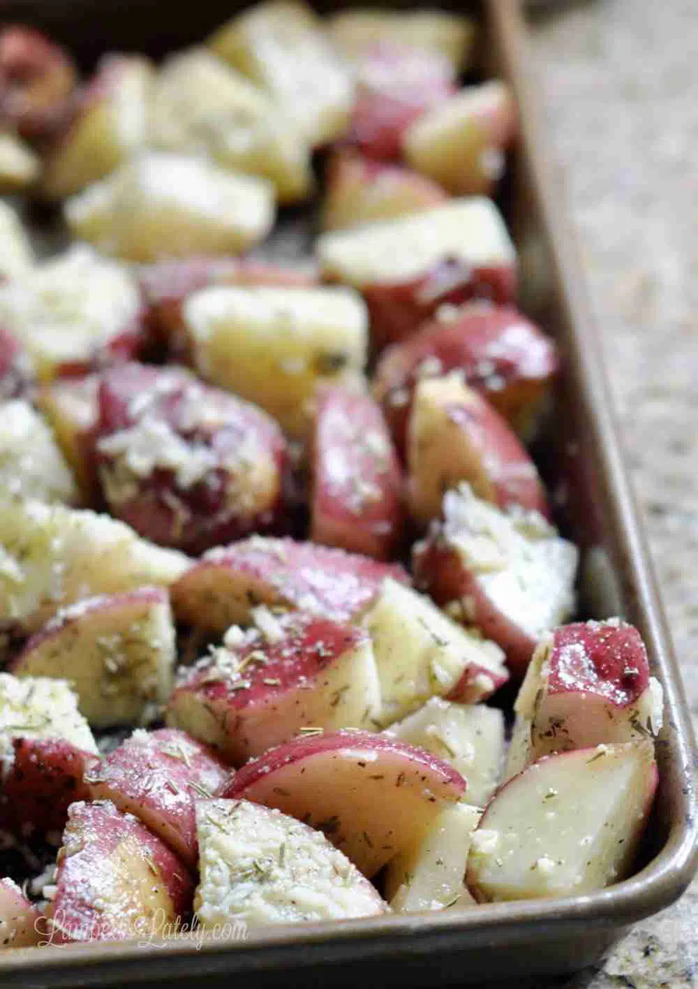 potato pieces on a baking sheet with rosemary, olive oil, parmesan, salt, and pepper