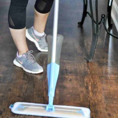 a view of lower legs and feet of a person holding a mop on lvp flooring.