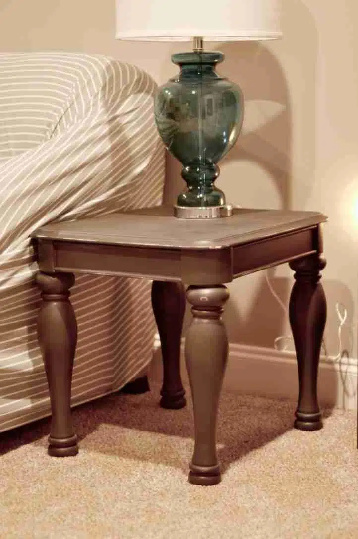 gray end table next to a couch, with lamp on top.