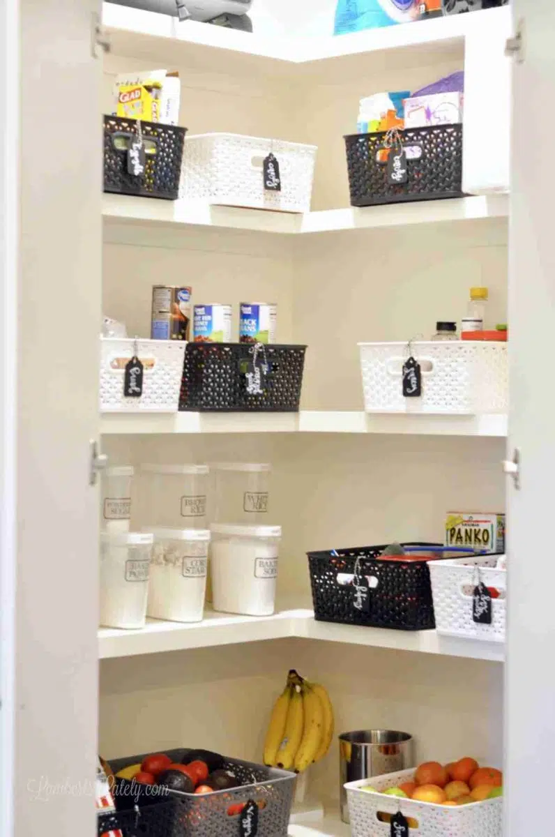 organized pantry with white, black, and gray plastic bins on shelves.