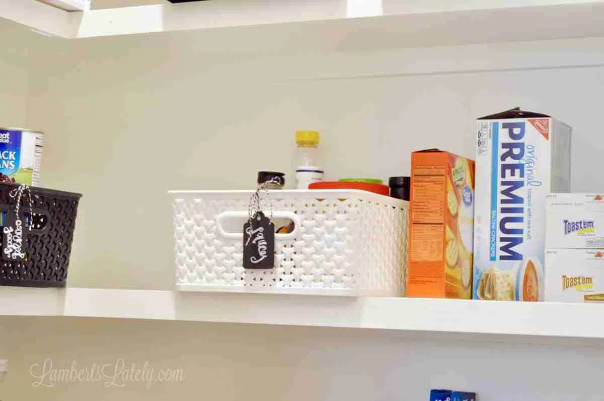 shelf of a pantry, with plastic bins and food boxes.