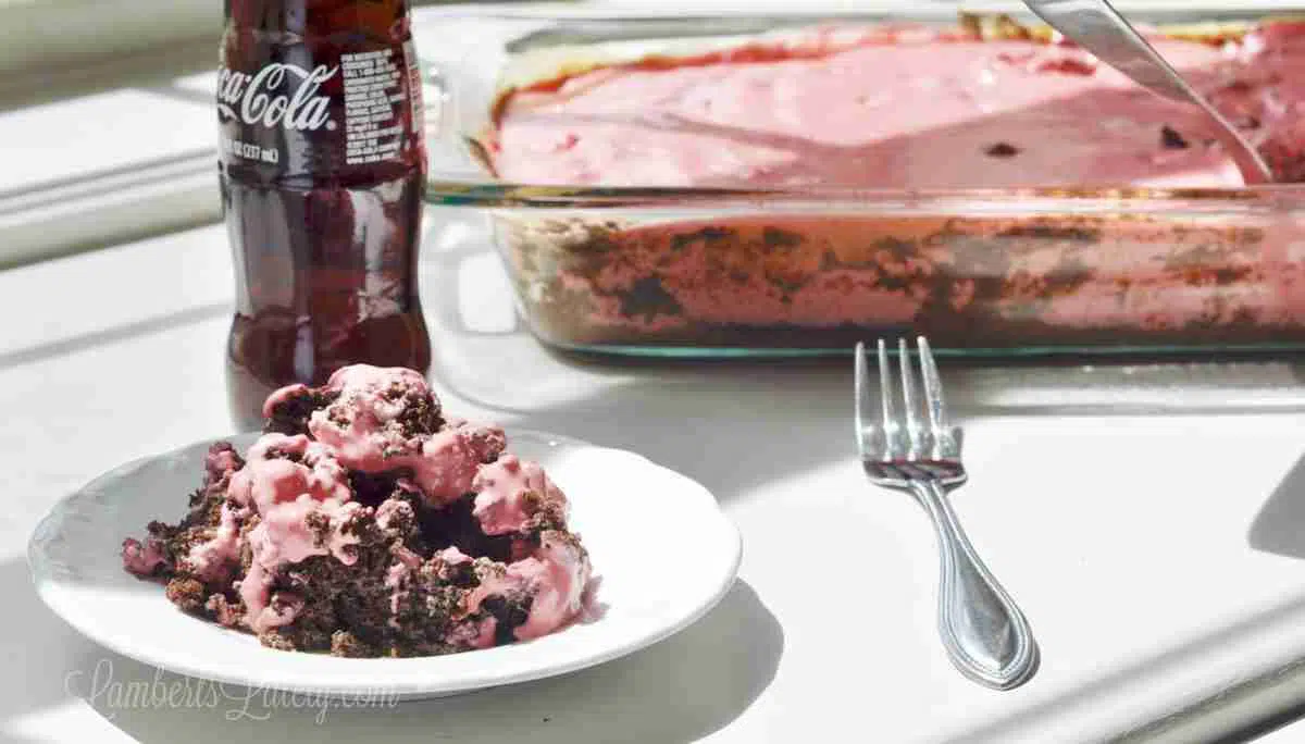 cherry coke earthquake cake on a white plate, with glass bottle of coke and baking dish.