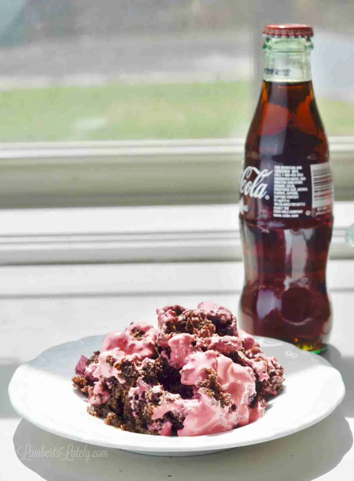 cherry coke earthquake cake on a white plate, with a glass bottle of coca cola.