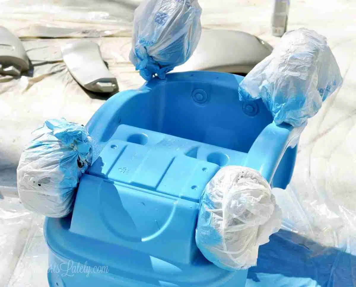 cozy coupe base turned upside down, wheels wrapped in plastic shopping bags, after painting blue.