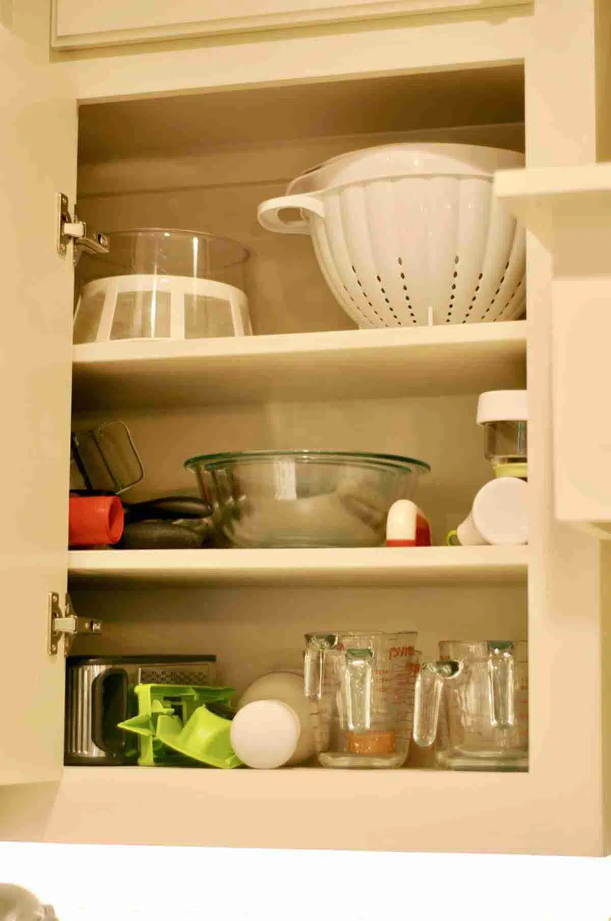kitchen cabinet with bowls, measuring cups, colander.