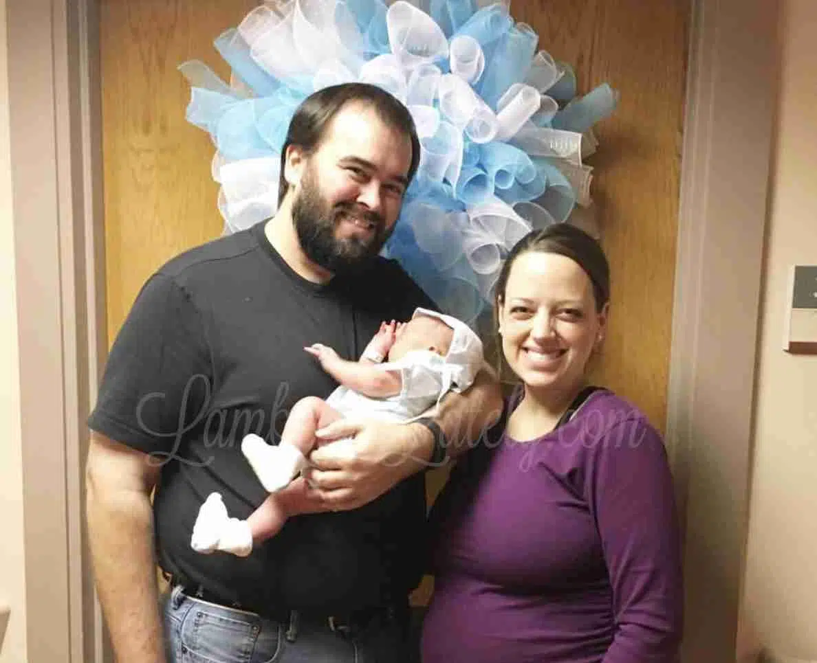 family with small baby in front of a hospital door with a wreath.