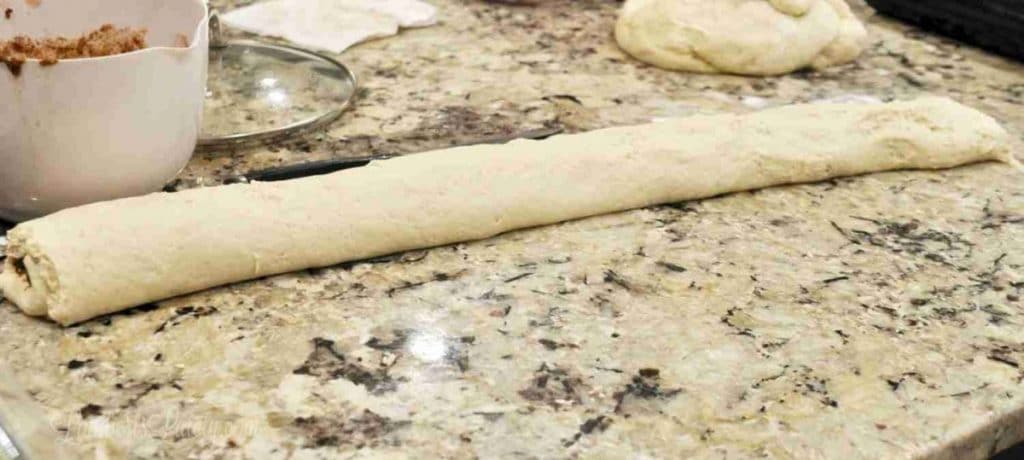 Unrolled cinnamon roll dough on a granite countertop for baking.