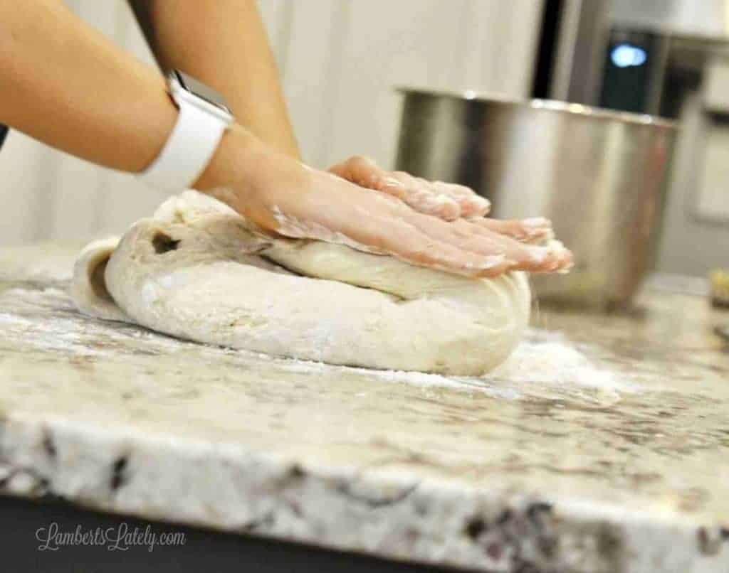 Person kneading dough on a marble countertop for cinnamon rolls.
