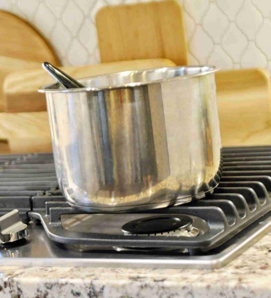 Stainless steel pot on stovetop with wooden cutting boards in background.