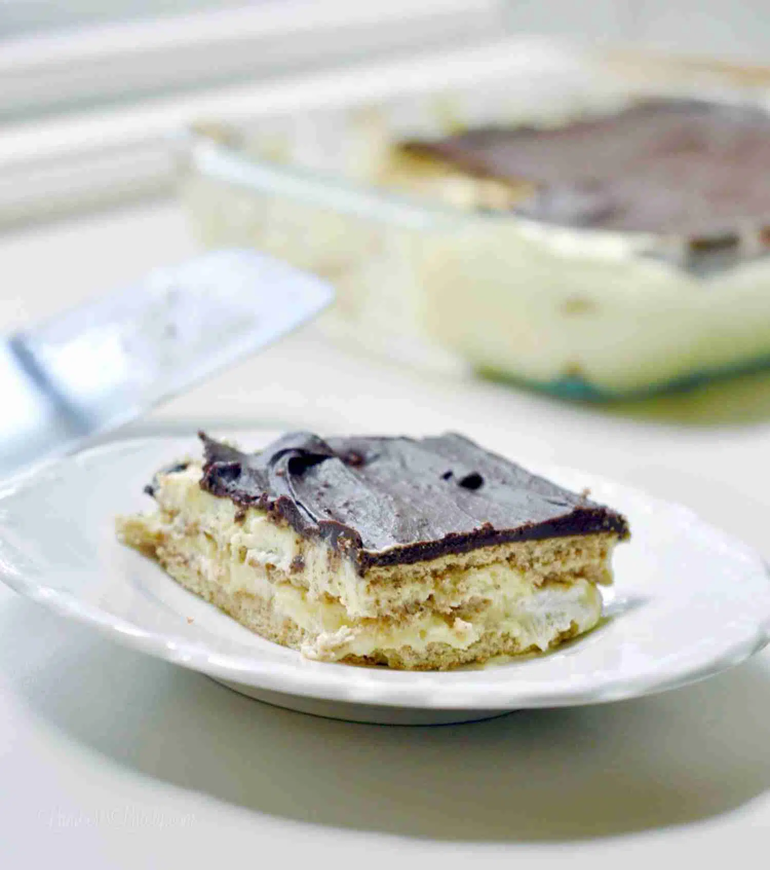 serving of chocolate eclair cake on a white plate, with baking dish in background.