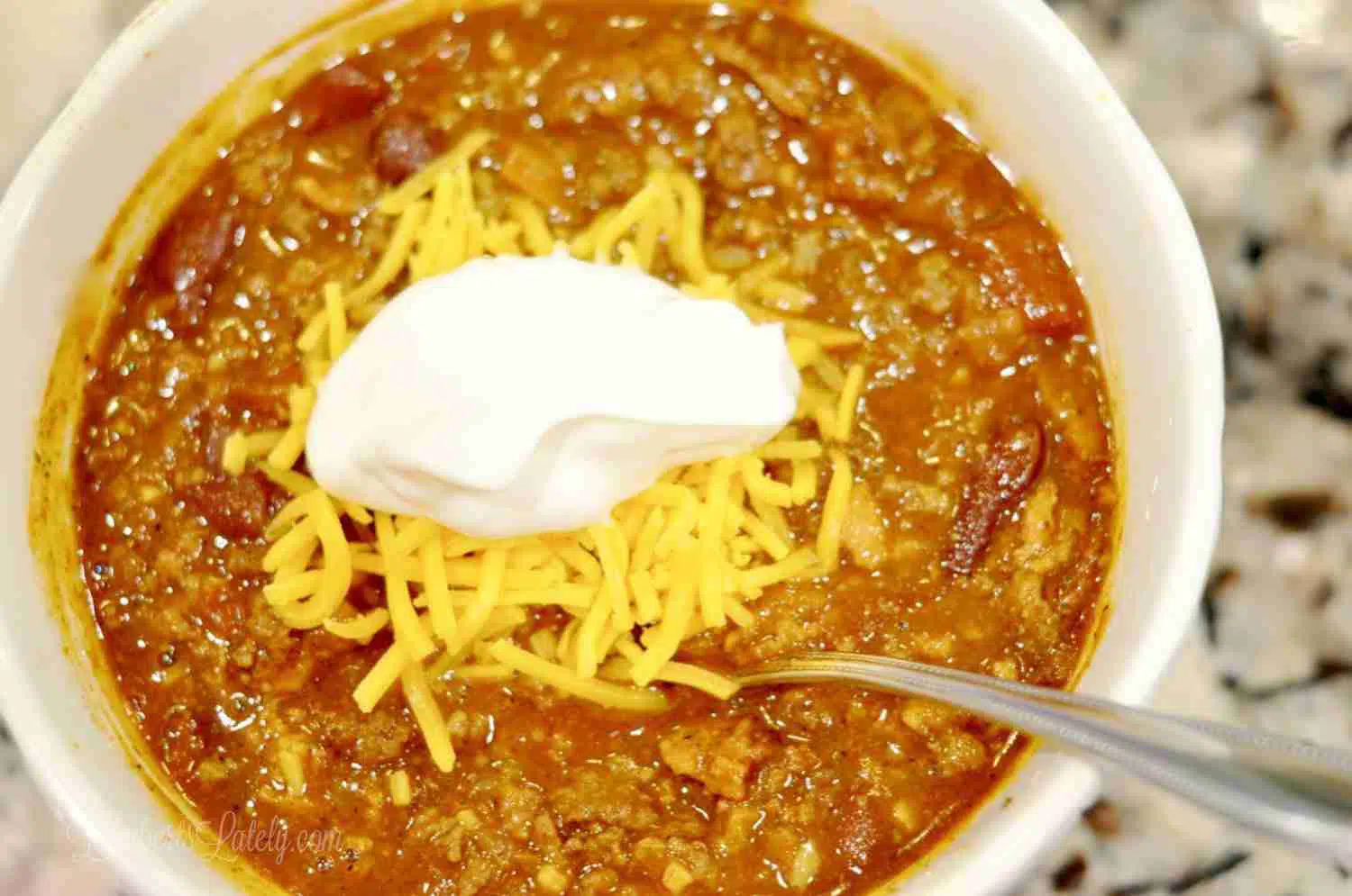 bowl of chili with sour cream and cheese on top.