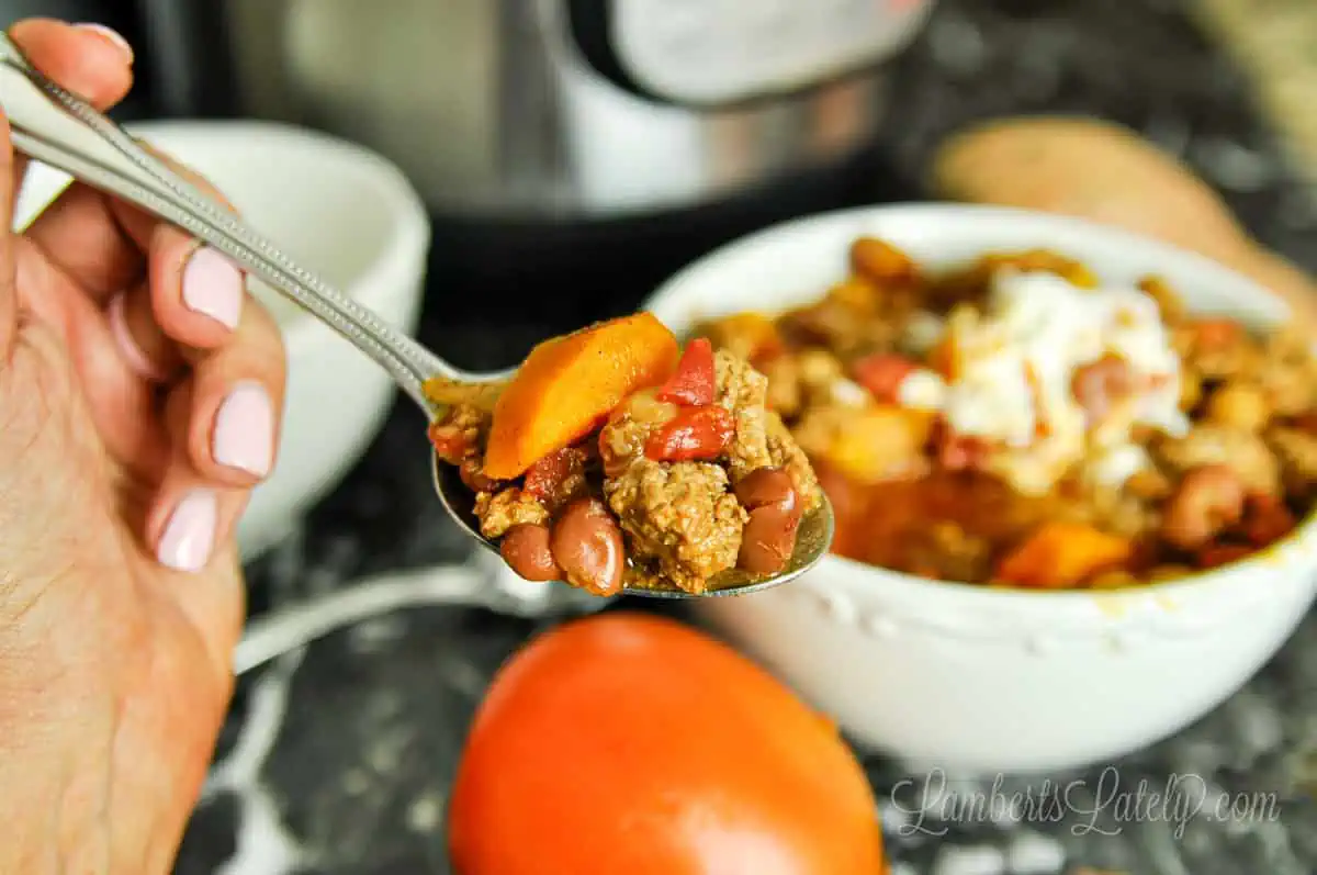 holding a spoon of turkey chili, showing tomatoes, beans, and sweet potatoes.