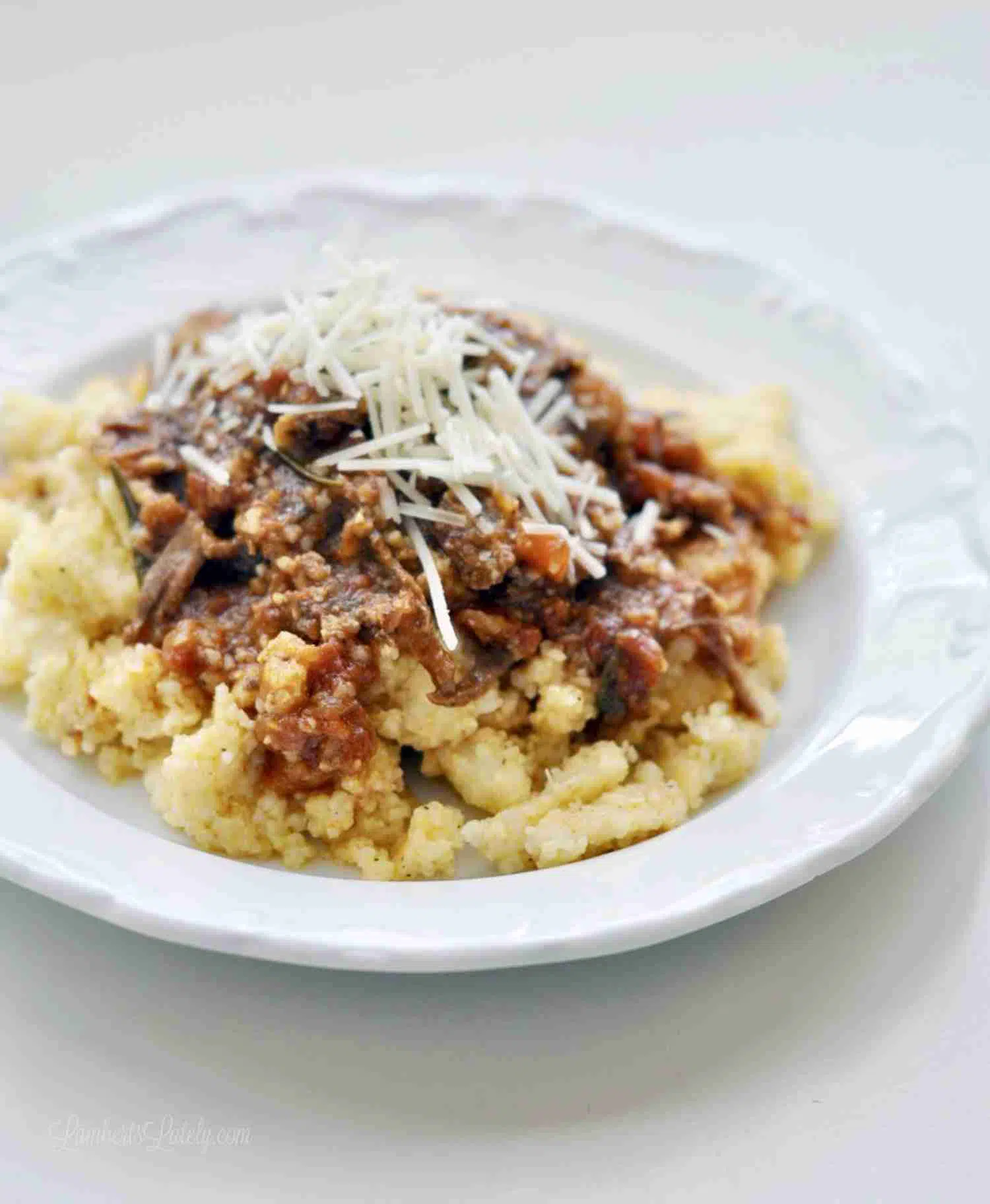 beef ragu over cheese grits, topped with shredded parmesan, on a white plate.