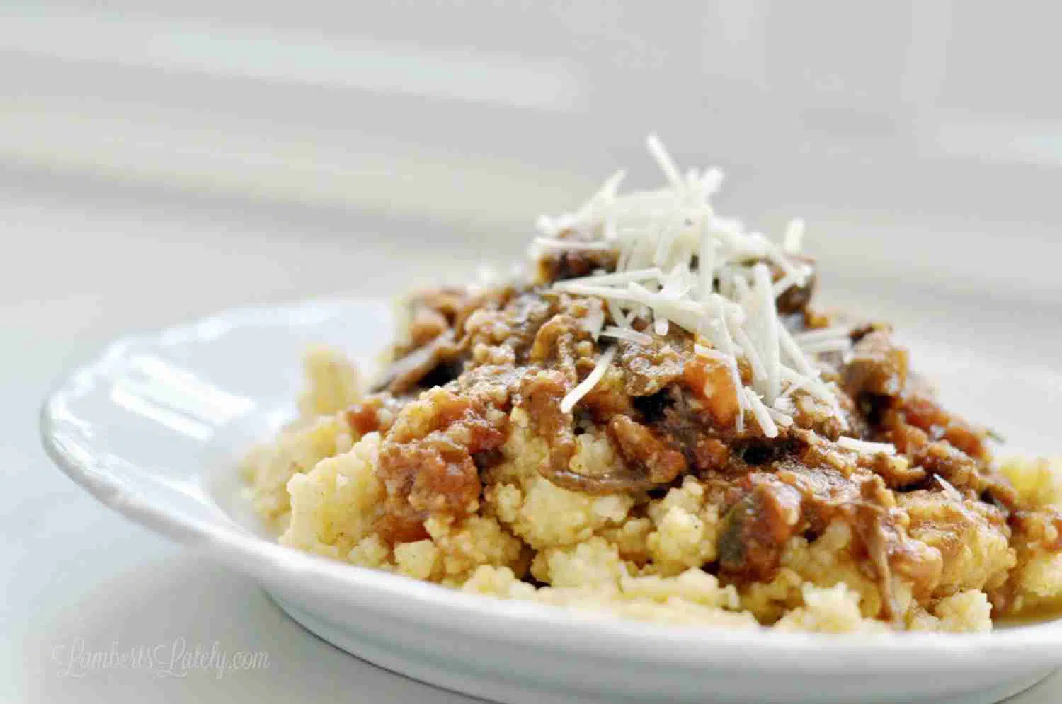 beef ragu over cheese grits, topped with shredded parmesan, on a white plate.