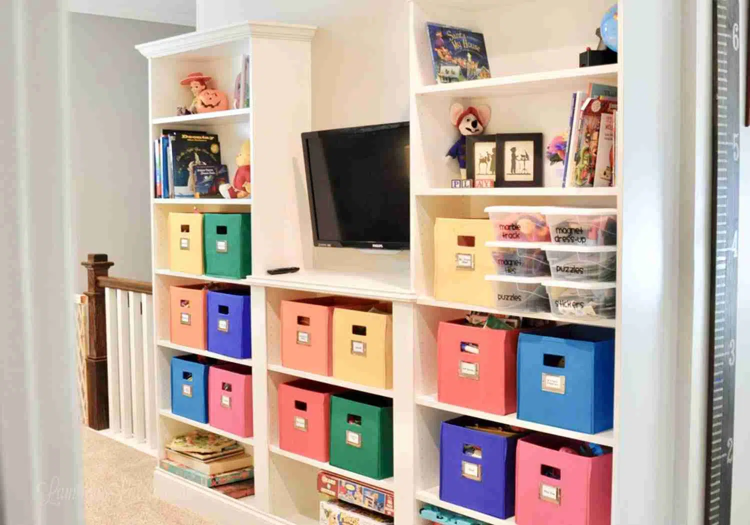 brightly colored bins, books, decor on white shelves, with a tv.
