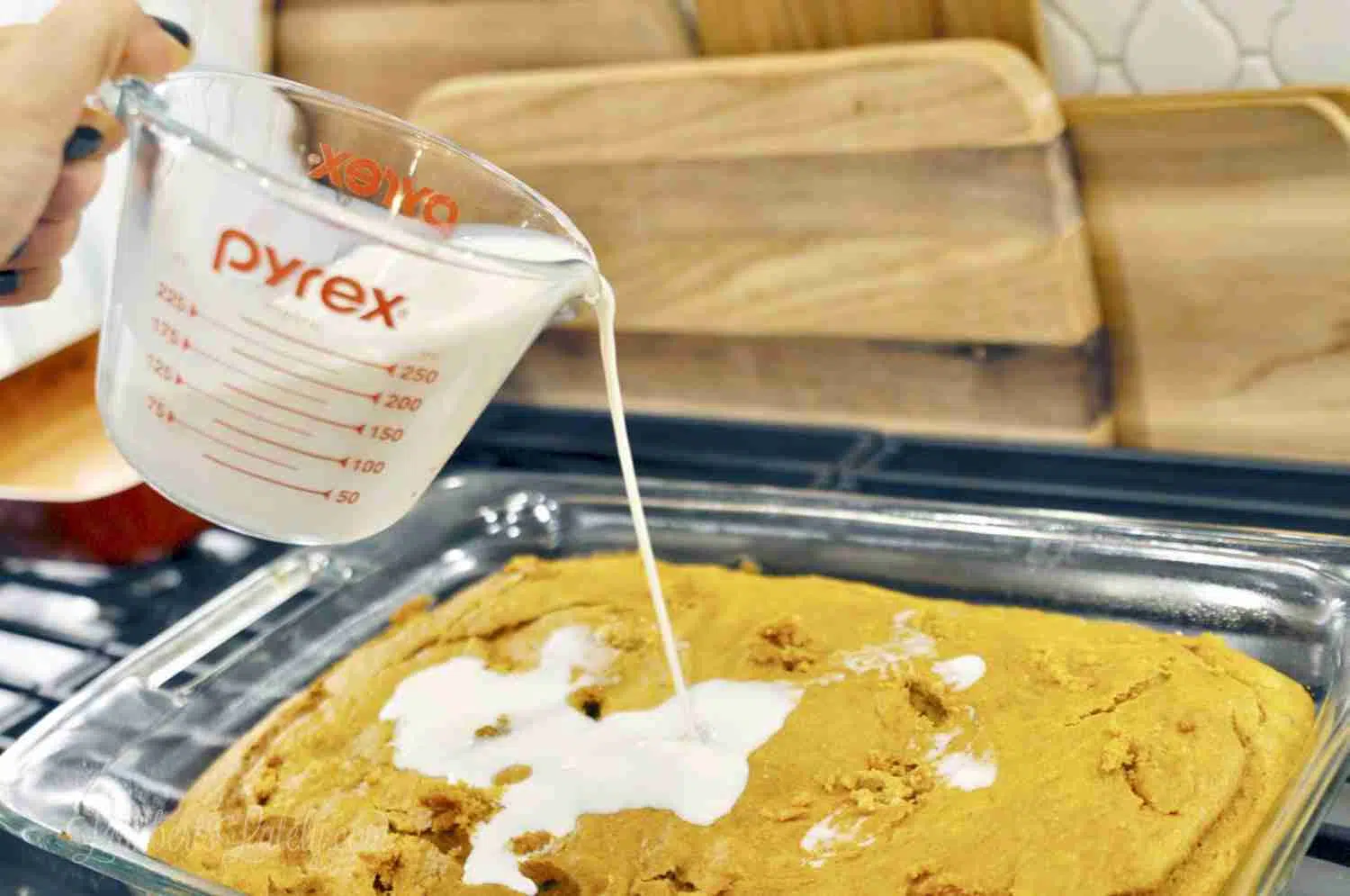 pouring sweet cream over a pumpkin cake in a baking dish.