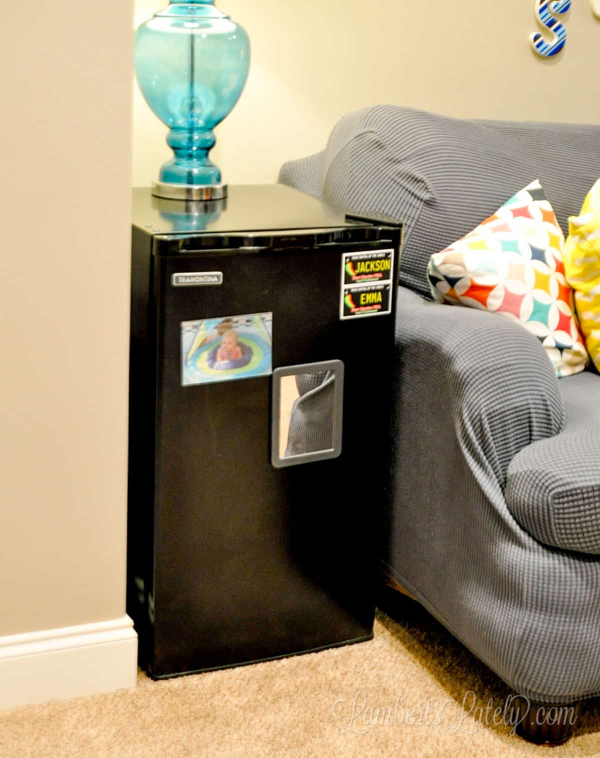 mini refrigerator with lamp on top next to a couch in a small playroom.