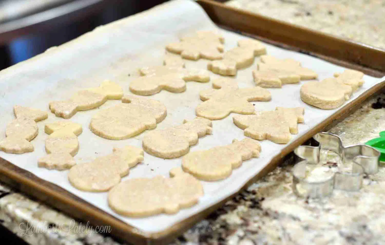 sugar cookies cut into christmas shapes on parchment paper lined baking sheet.