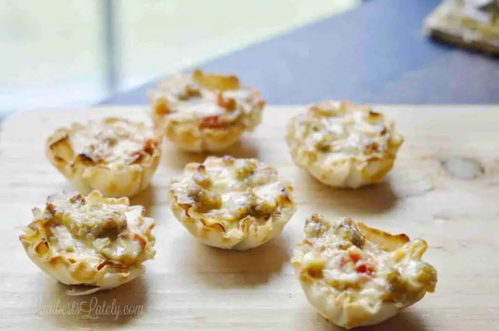 six individual sausage phyllo cups laid out on a wood counter.