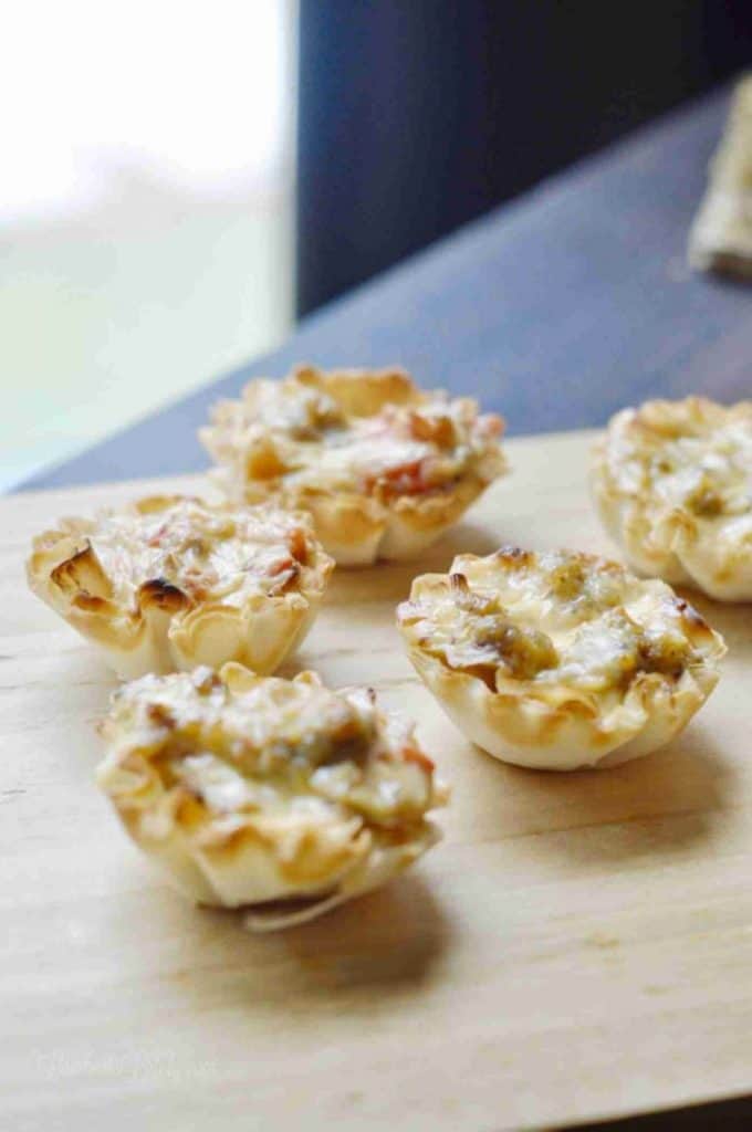 phyllo cups filled with cheese and sausage on a cutting board