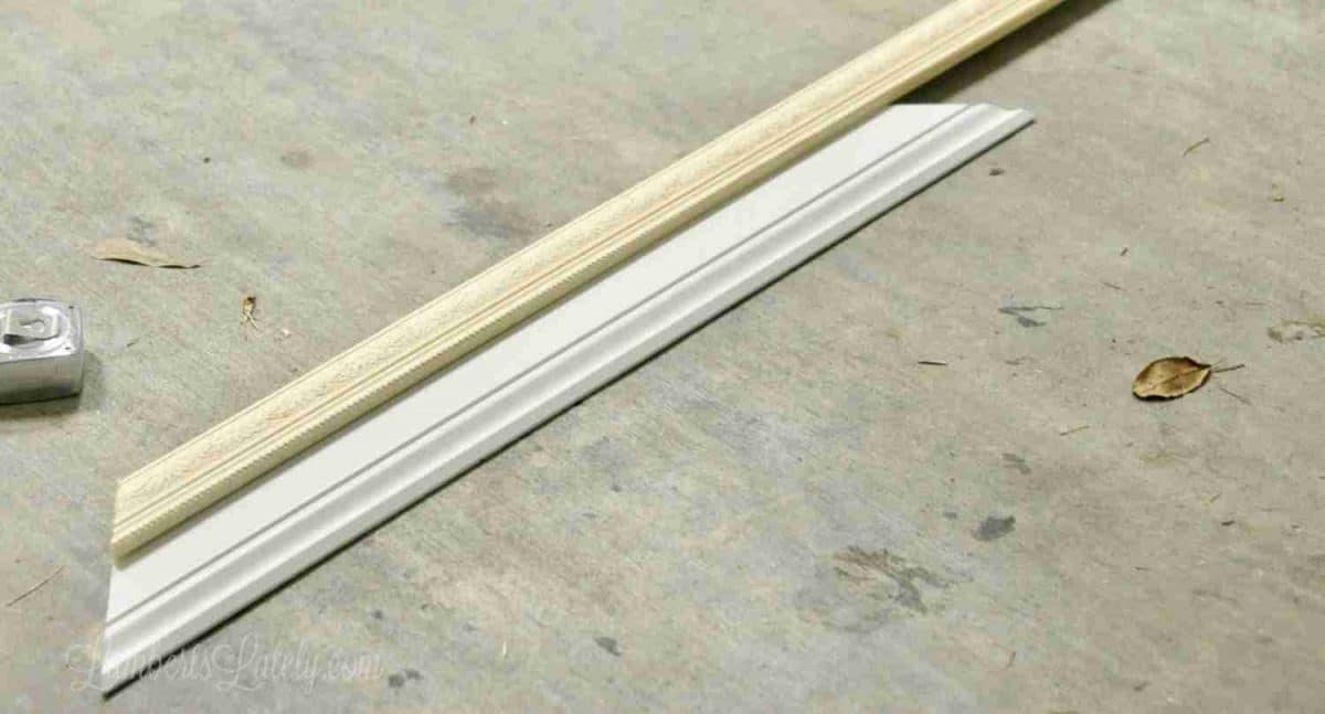 two pieces of molding and a measuring tape laying on a garage floor, one on top of the other.
