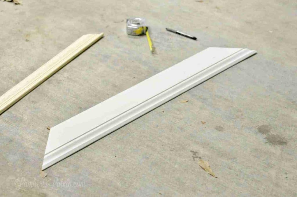 measuring tape, pen, two pieces of molding laying a on a garage floor.