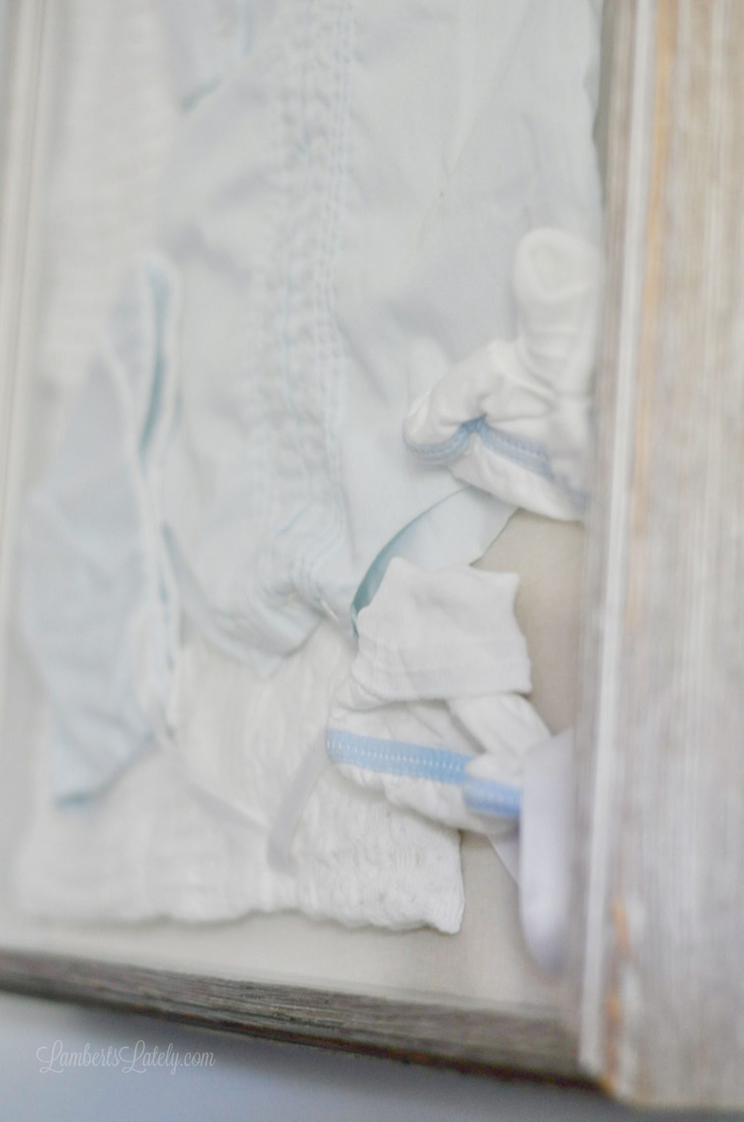 close up corner of a shadow box with a baby outfit.