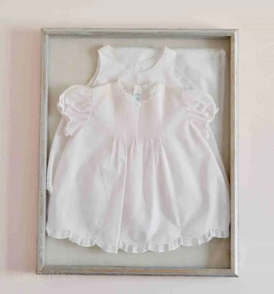 pink newborn baby dress framed in a shadow box on a wall.