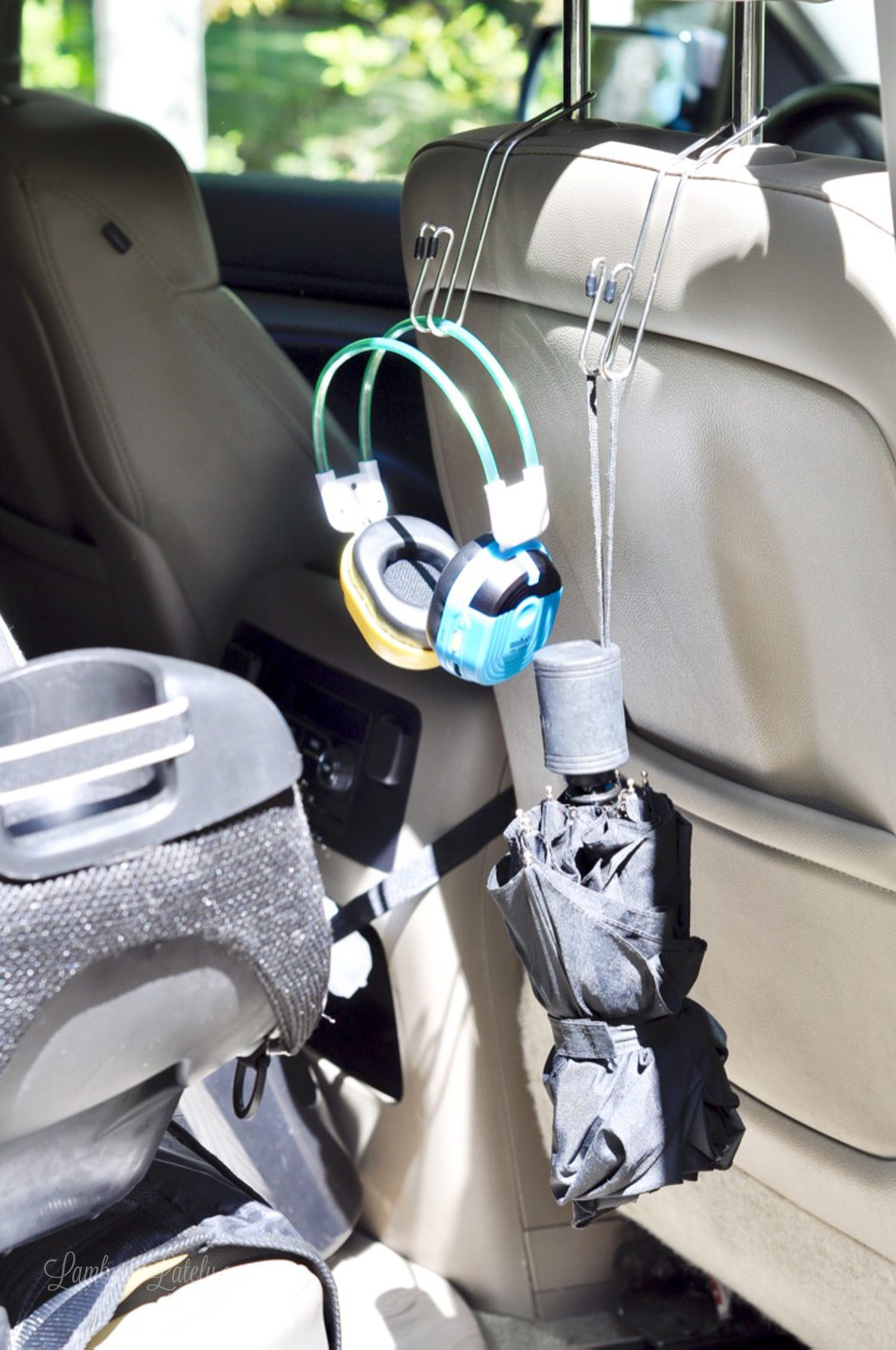 headphones and umbrella hanging on the back of a car seat with metal hangers.