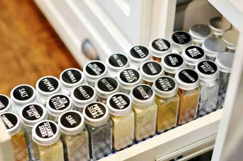open spice cabinet with black glass spice jars lined in rows.