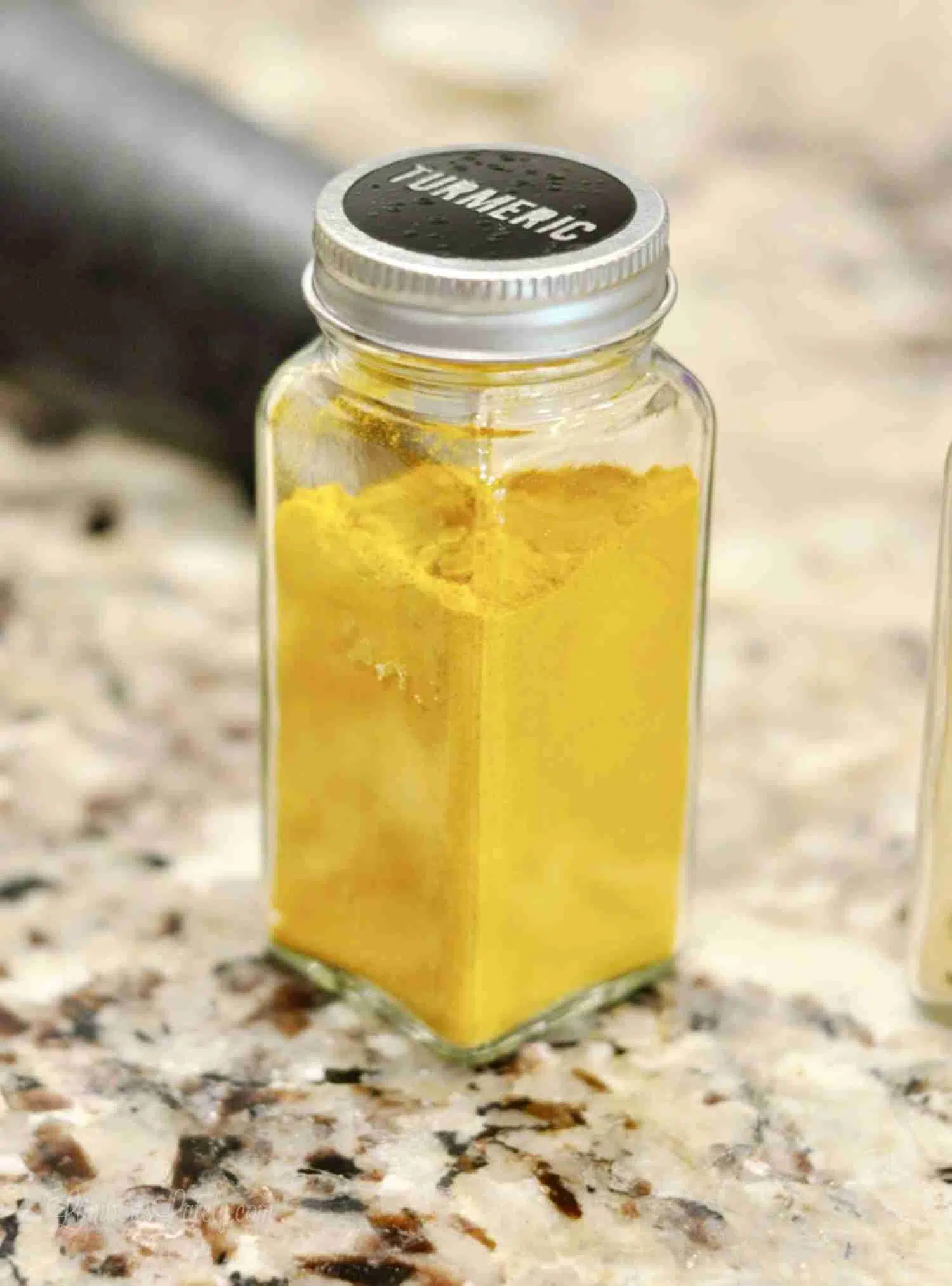 yellow turmeric in a glass spice jar with a black label on top.