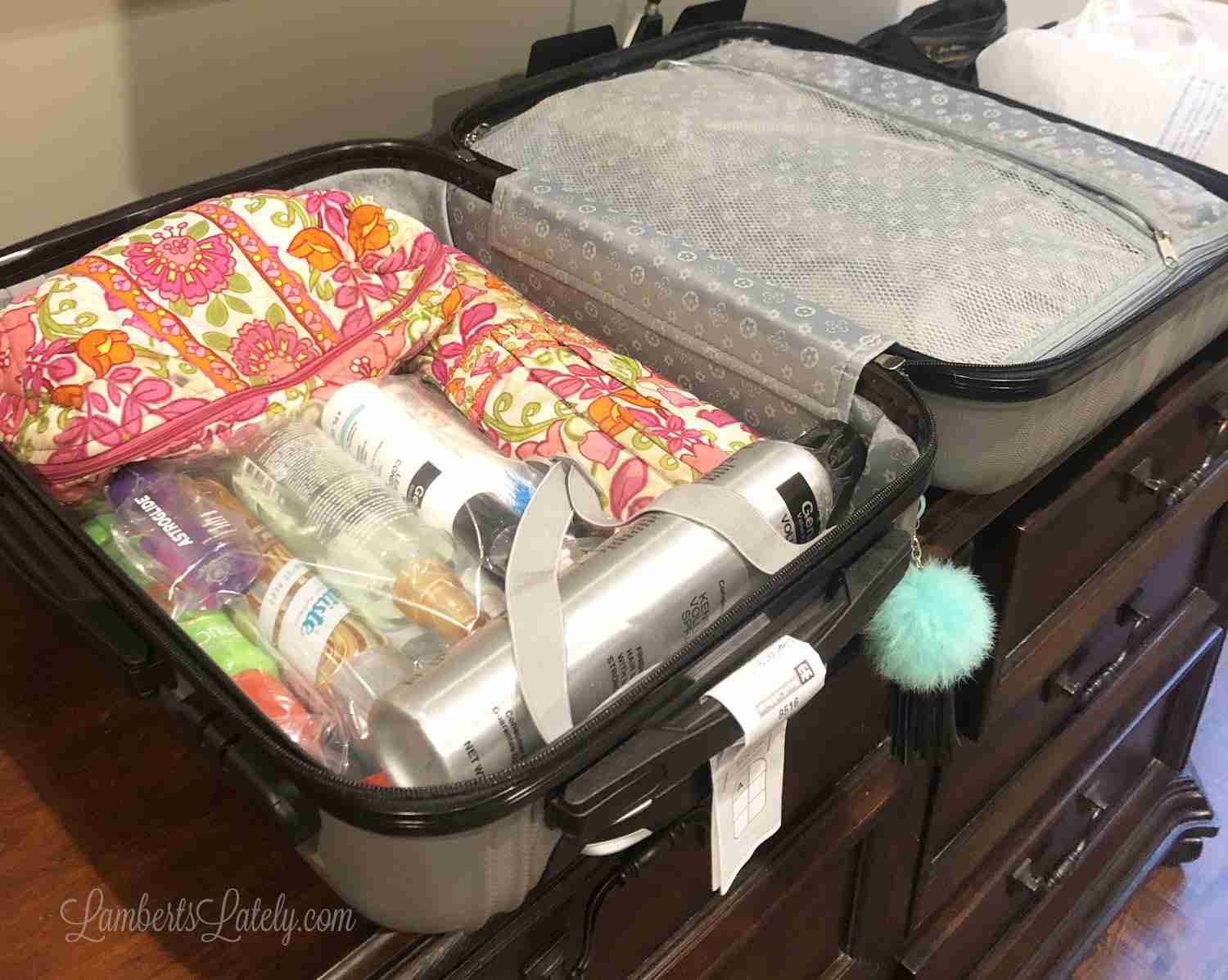 suitcase packed with pink floral toiletry bags and plastic bags for bottles.