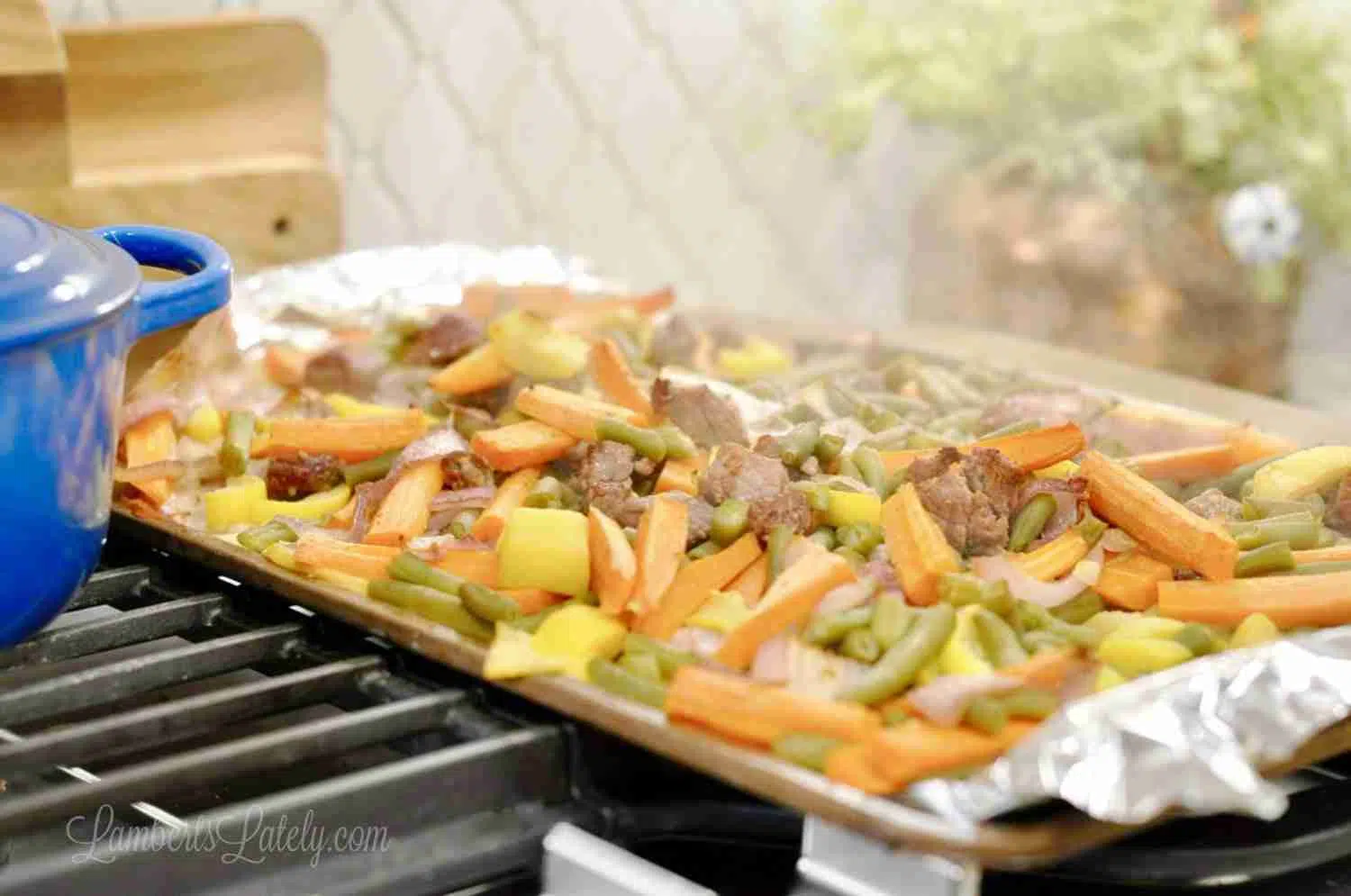 beef and colorful vegetables on a foil-lined sheet pan, sitting on a stovetop.