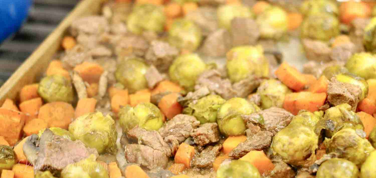 steak, chopped carrots, and brussels sprouts on a sheet pan.