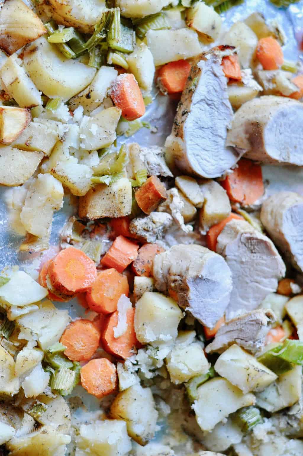 pork tenderloin, carrots, celery, and apples on a sheet pan.