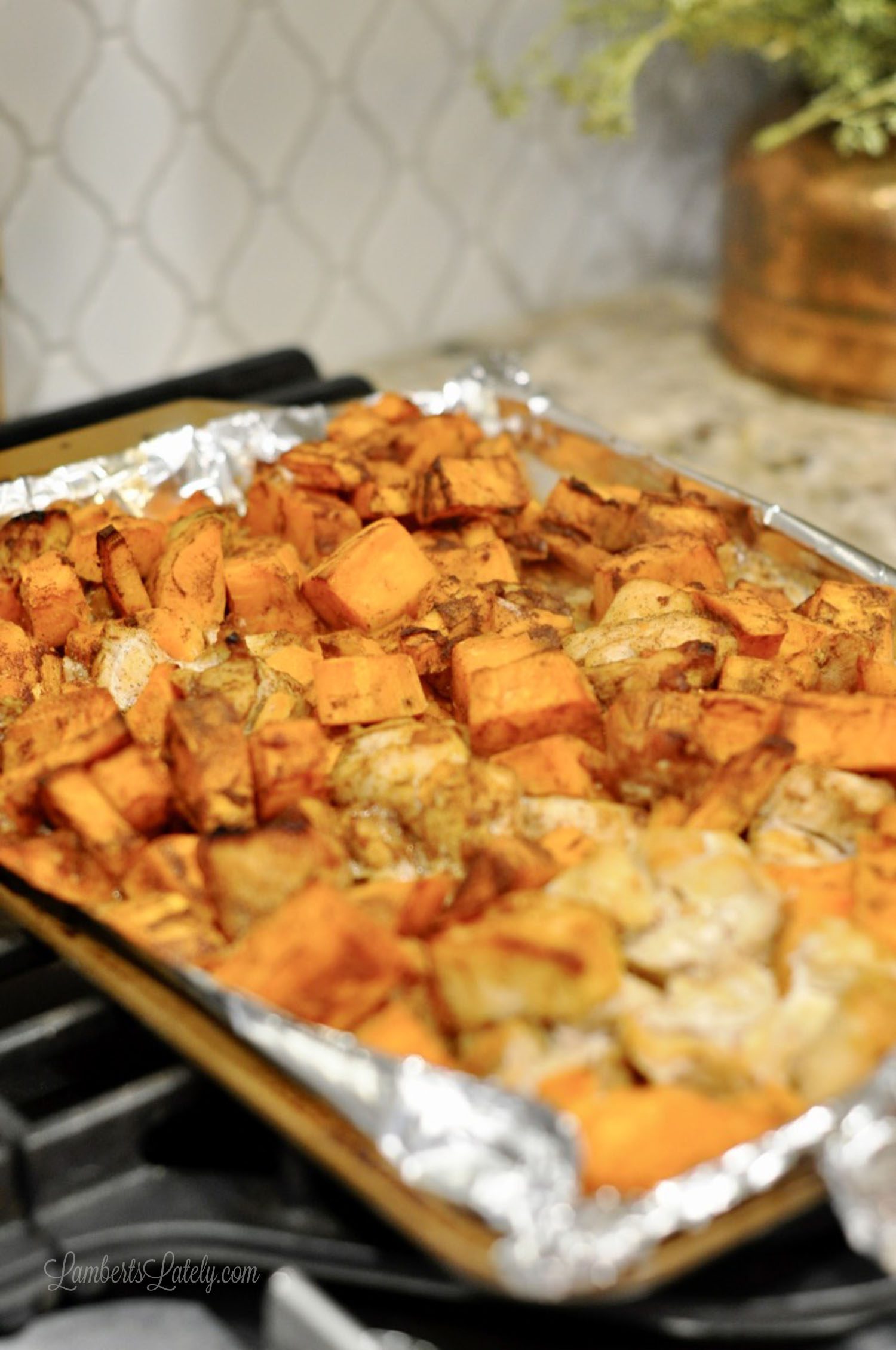 chicken and sweet potatoes on a sheet pan lined with foil on a stove.