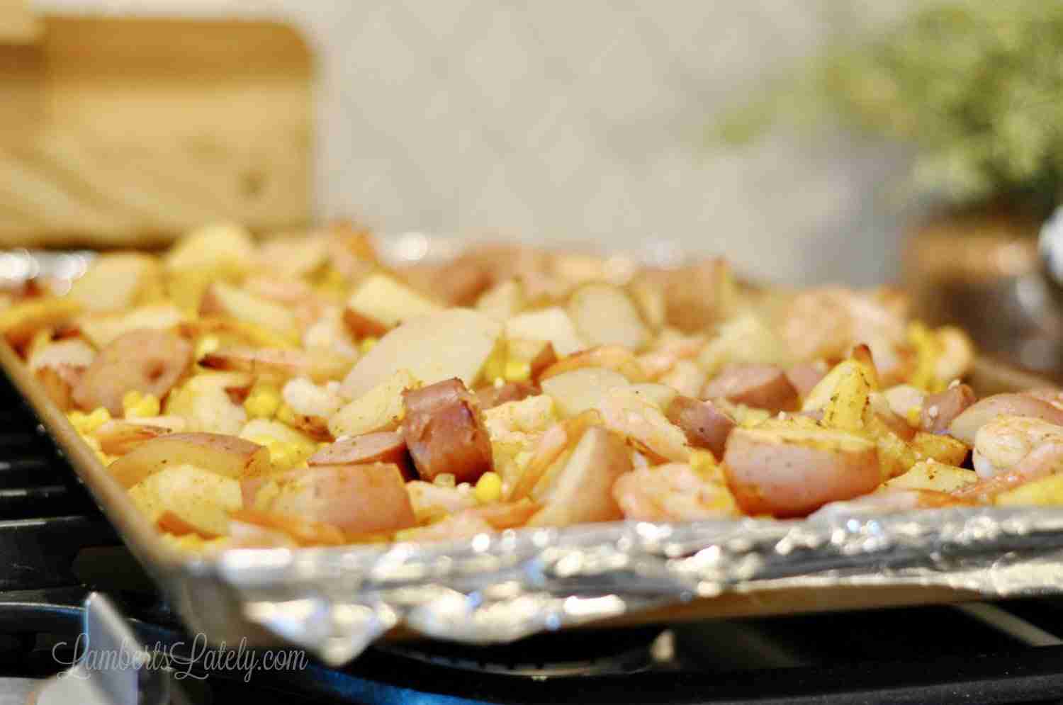 shrimp, sausage, lemon, and potatoes on a sheet pan lined with foil on a stovetop.