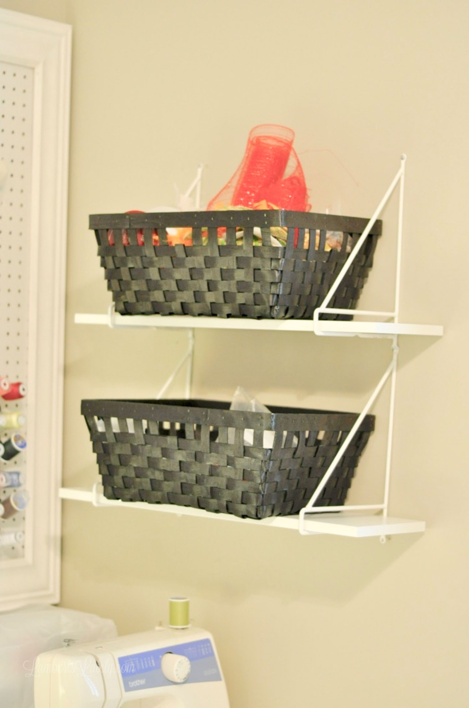 two black baskets holding craft supplies on white shelves.