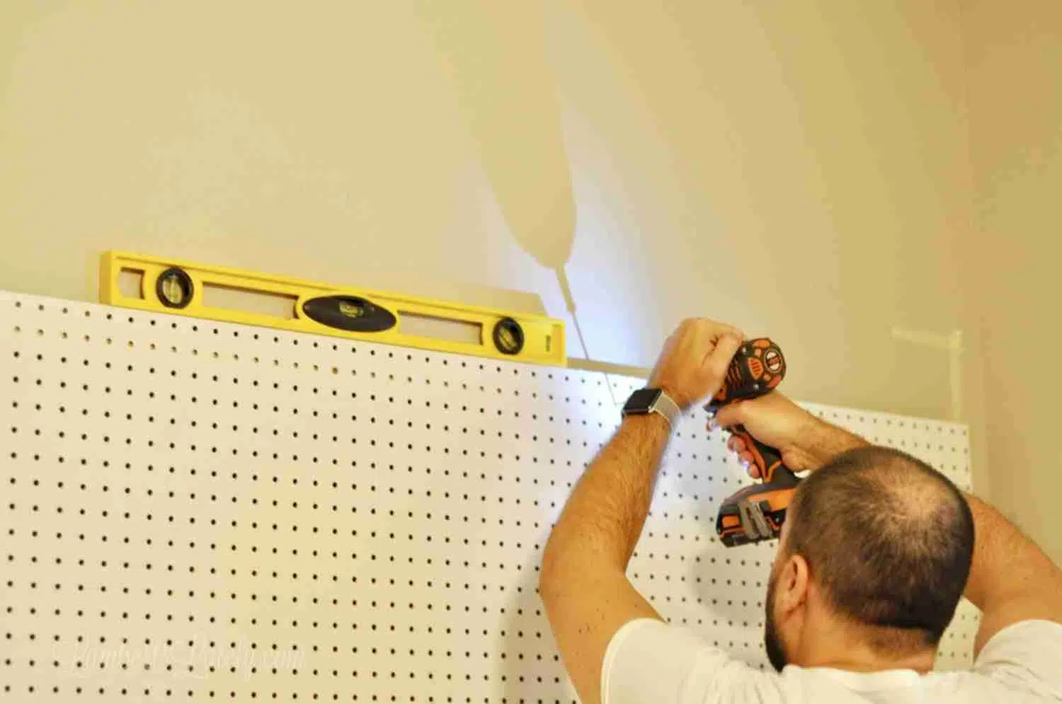 level sitting on top of pegboard, man drilling board into wall