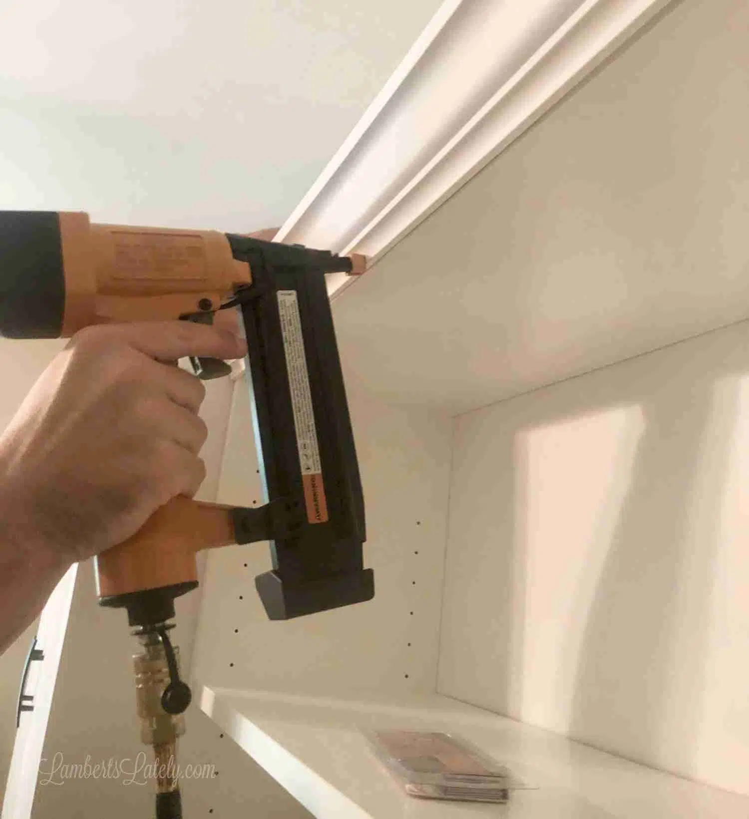 using a pneumatic nail gun to install crown molding on a shelf.