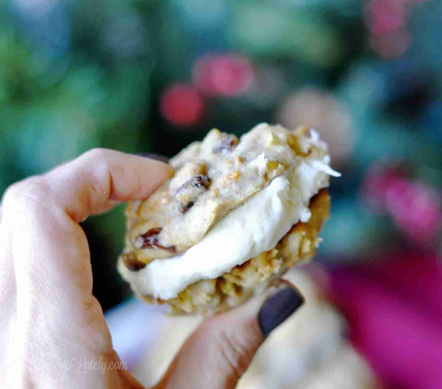 holding a carrot cake sandwich cookie with a bite missing.