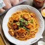 Spaghetti with chicken, green onions, and chili onion crunch sauce on a white plate.