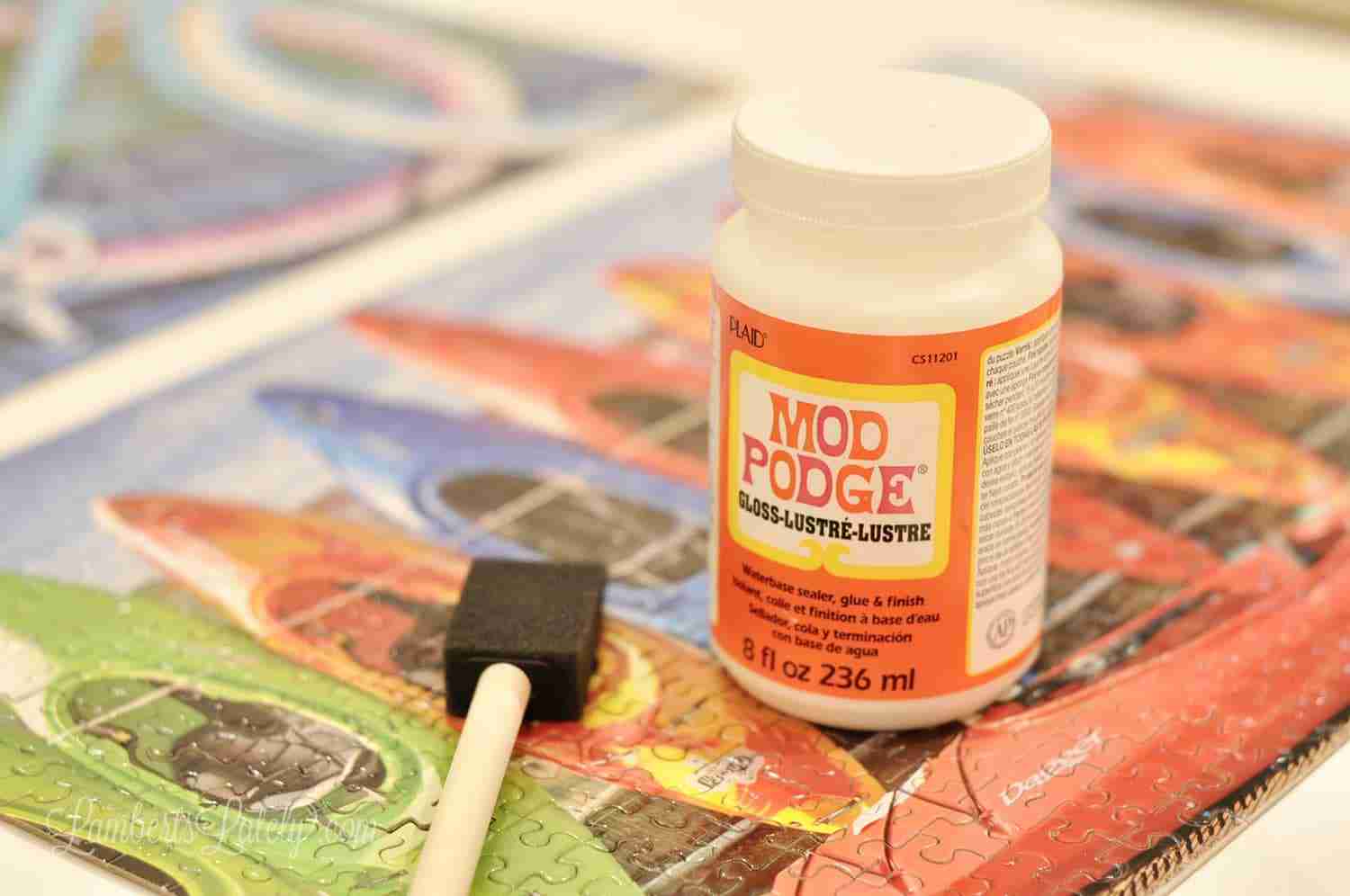 bottle of mod podge and a sponge brush on a puzzle