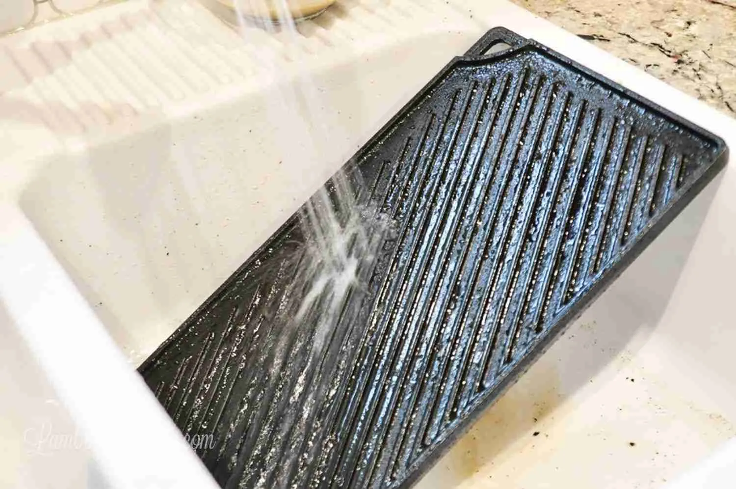 spraying water on a cast iron griddle in a sink